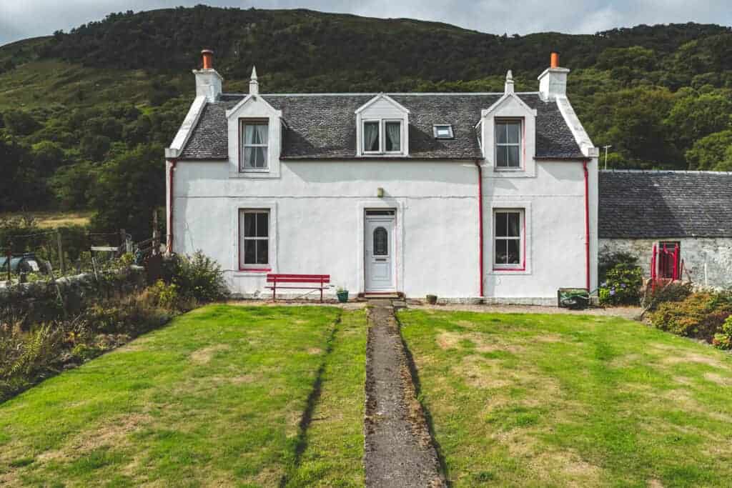 Charming white cottage with traditional architecture, surrounded by greenery and scenic hills, perfect for property investment or a cosy home.
