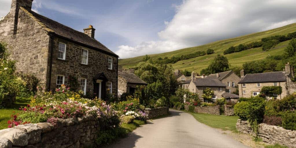 Charming countryside stone cottages with lush gardens in a scenic rural village, surrounded by rolling green hills and vibrant wildflowers, exemplifying peaceful property living in England.