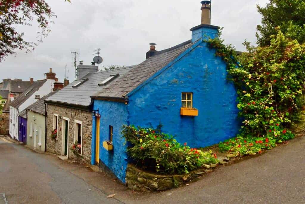 Colourful blue cottage with a stone wall exterior on a quaint street in the UK, surrounded by lush greenery and vibrant flowers, showcasing charming residential property for property management services.