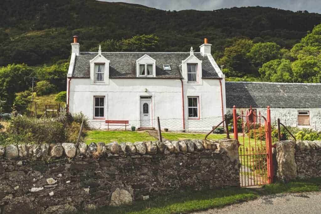 Charming white cottage with traditional architecture, surrounded by lush greenery and hills, perfect for property investment, refurbishment, or as a cosy countryside retreat.