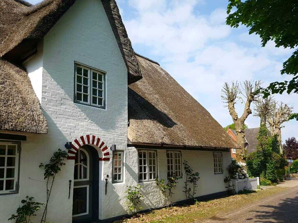 Charming English thatched cottage with white brick walls, leaded windows, surrounded by a peaceful countryside setting and clear sky.