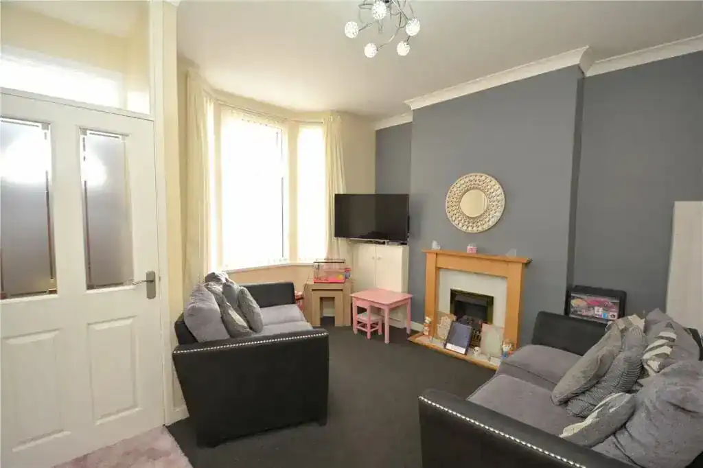A cosy living room featuring grey walls, two black sofas, a fireplace, and a wall-mounted TV, ideal for comfortable family gatherings in an affordable English home.