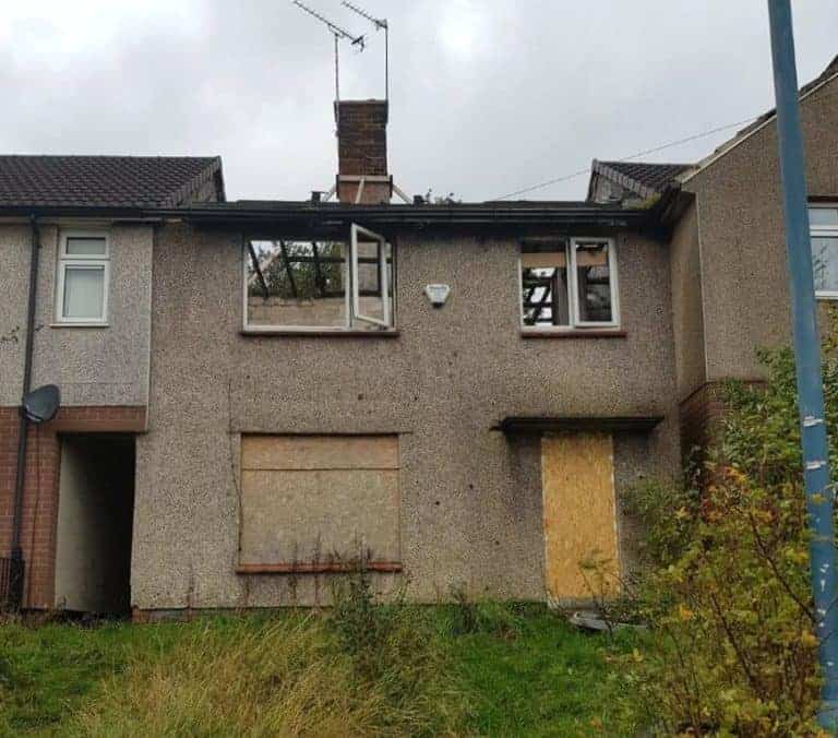 Fire damaged house with boarded windows and visible structural damage