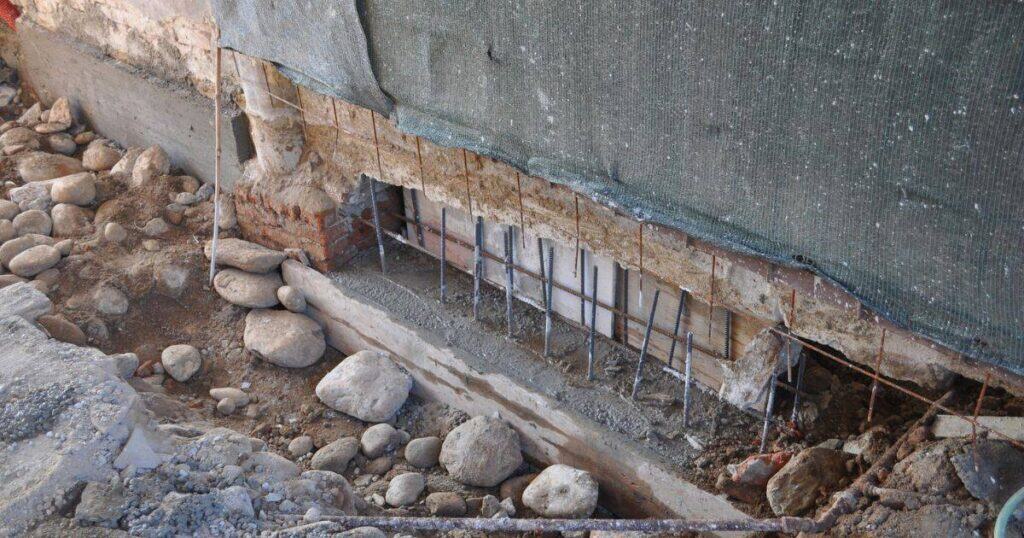 Close-up of a damaged underpinning wall with exposed rebar and crumbling concrete, highlighting the importance of professional underpinning solutions for property stability.