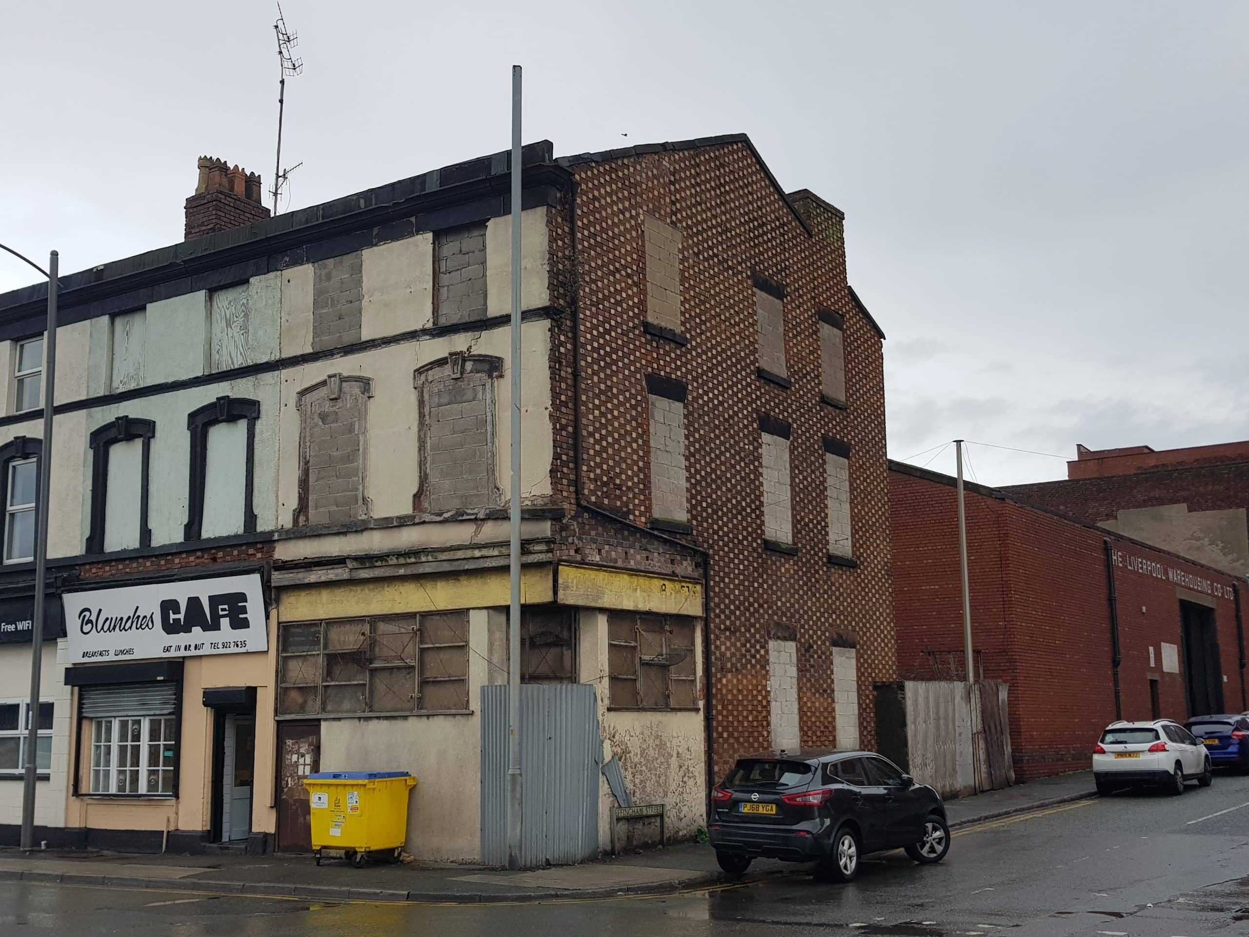 Boarded-up urban building with faded cafe sign next to a parked car on a wet street.