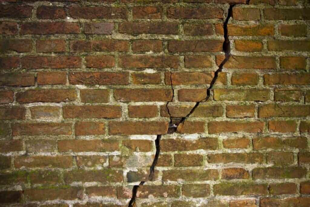 Close-up of a cracked brick wall highlighting structural issues in a property. Ideal for illustrating house damage and the importance of professional assessment before selling.