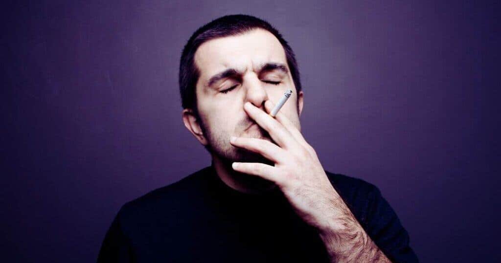 Man smoking a cigarette with a smoky background, illustrating the impact of smoking on property value and cleanliness.